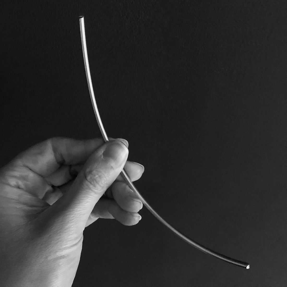black and white image of large piece of thick gold wire hold by a hand